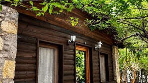 A rustic wooden cabin with stone walls, a wooden door, and windows with curtains. - Petrinos Butik Otel (Datça)