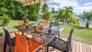 An outdoor dining area with a table set for two, surrounded by chairs, overlooking a tropical landscape with palm trees and a view of the ocean. - Éole, a charming villa, within walking distance of the beach, with a view of the sea (Sainte-Luce)