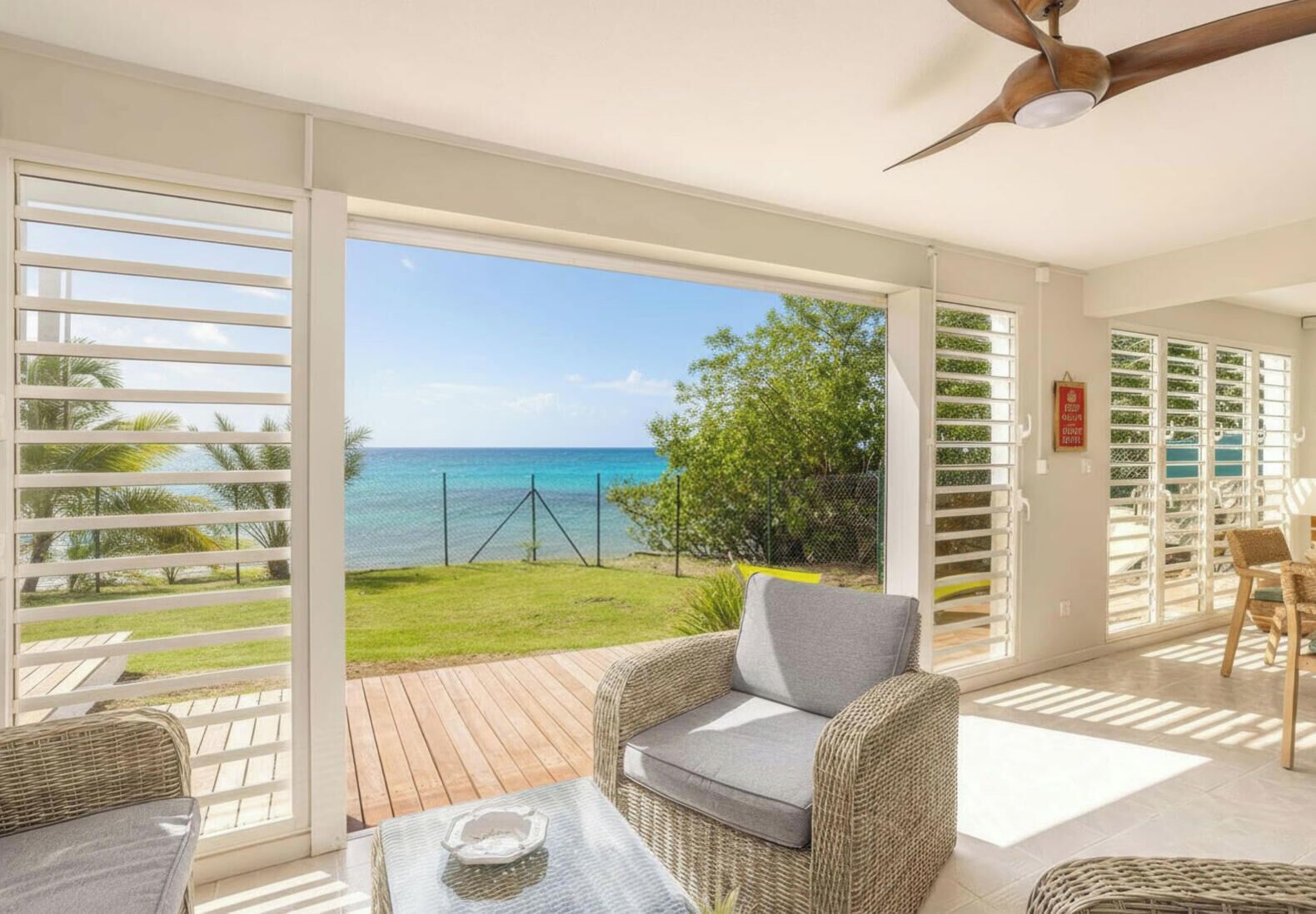 A room with a view of the ocean, a ceiling fan, and wicker furniture.