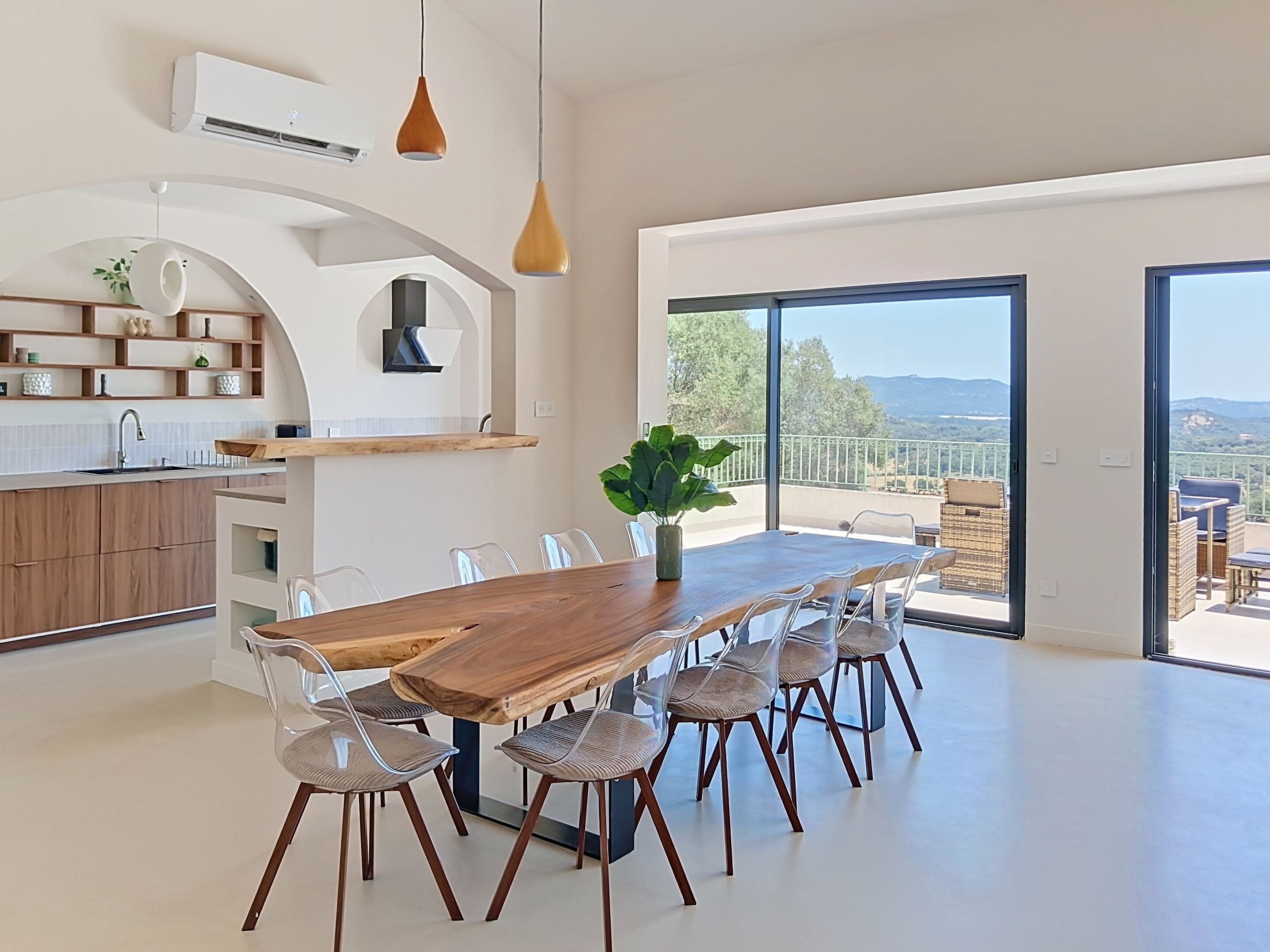 Una cocina moderna con una mesa y sillas de madera, un ventanal con vistas y un balcón con mobiliario exterior.