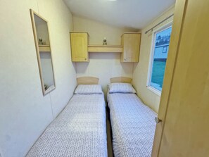 Un petit logement composé d’une seule pièce, comprenant deux lits, un miroir et une fenêtre.