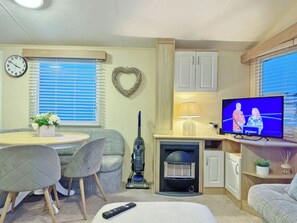 Un espace de vie compact comprenant un coin repas, un téléviseur, un aspirateur et un décor en forme de cœur accroché au mur.