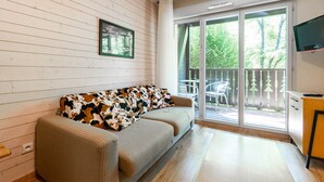 A room with a sofa, a television, and a sliding glass door leading to an outdoor area. - Flat balcony overlooking the countryside, close to shops (Ax-les-Thermes)