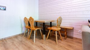 A room with a wooden table and four chairs, a bench, and a wall with horizontal wooden panels. - Flat balcony overlooking the countryside, close to shops (Ax-les-Thermes)