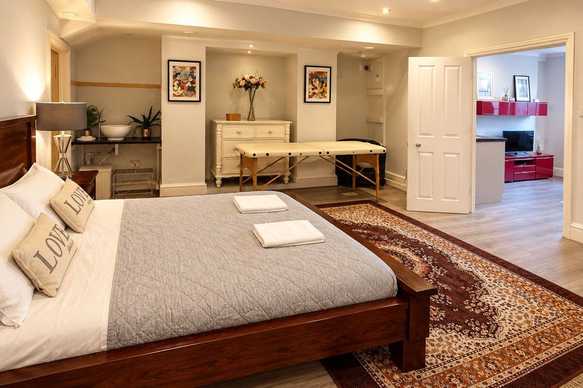 A bedroom with a bed, bedside tables, a nightstand, a desk, a chair, a dresser, a mirror, a door, and a rug.