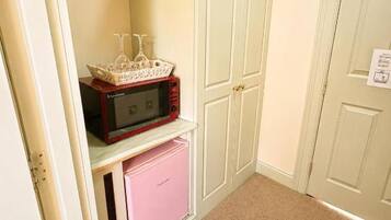 A room with a white door, a pink appliance, and a cabinet with a microwave on top.