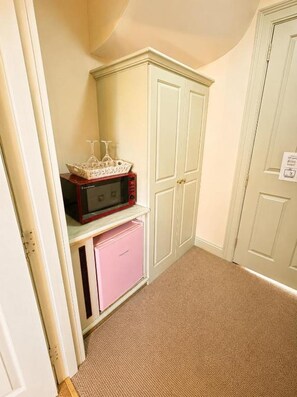 A room with a white door, a pink appliance, and a cabinet with a microwave on top. - 12A Regency Square (Brighton and Hove)