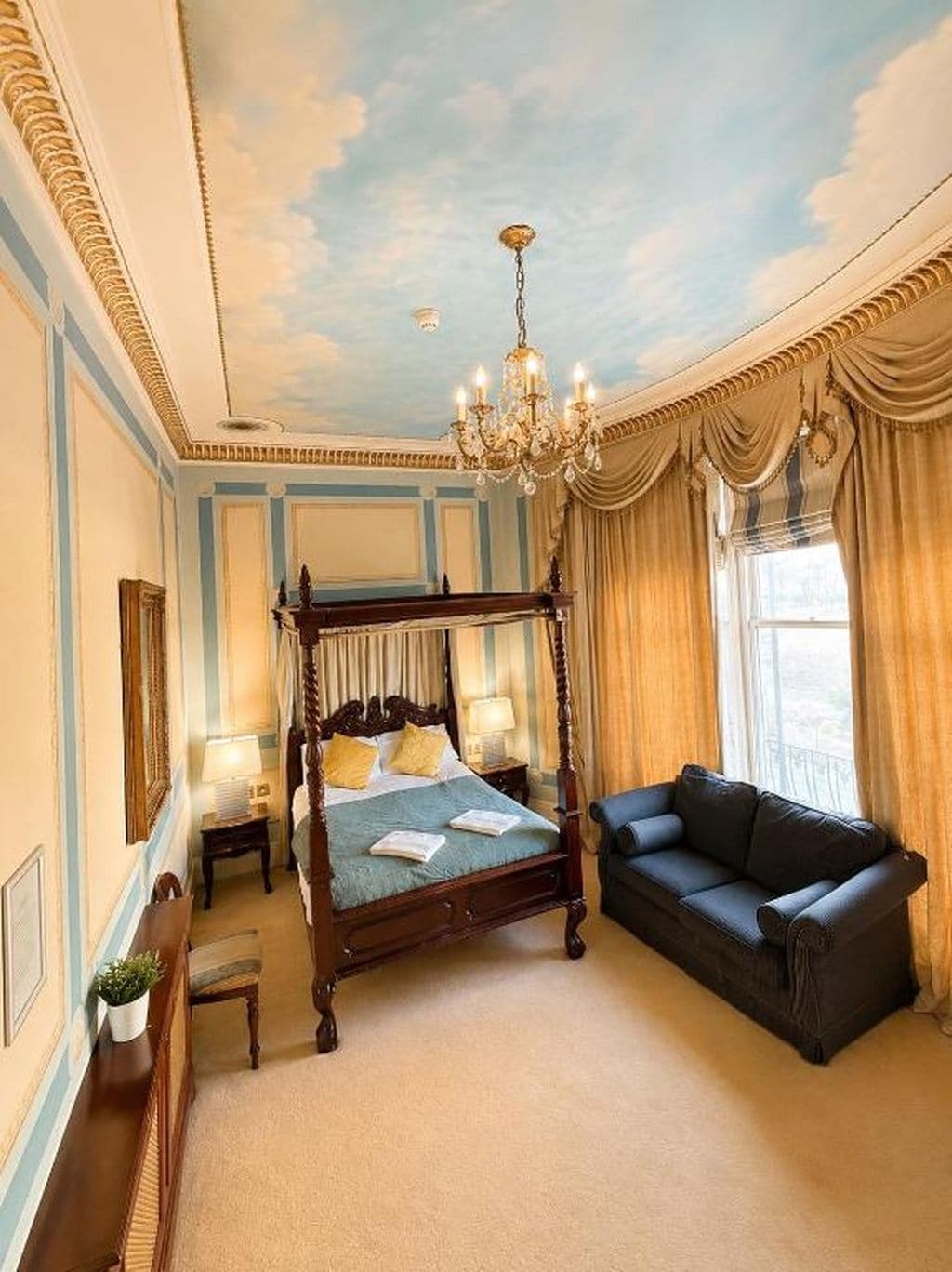 A four-poster bed with a canopy, a chandelier, a sofa, and a view of the outdoors.