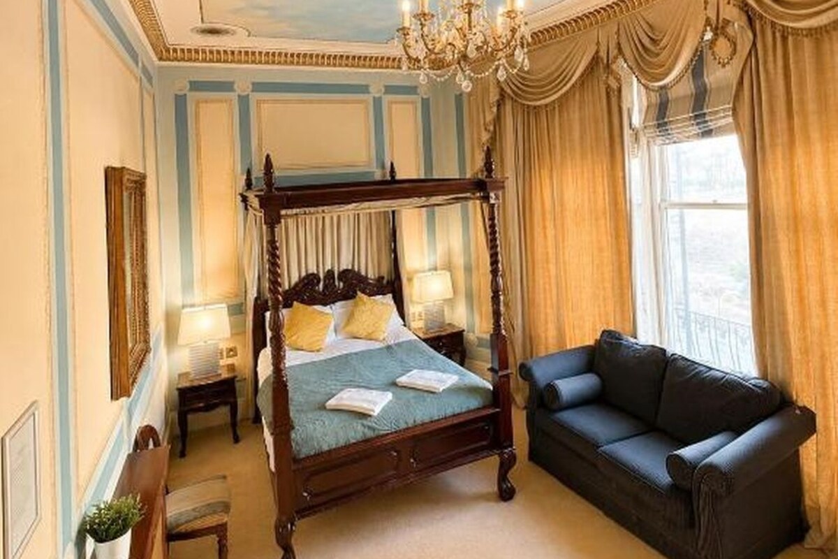 A four-poster bed with a canopy, a chandelier, a sofa, and a view of the outdoors.