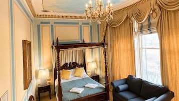 A four-poster bed with a canopy, a chandelier, a sofa, and a view of the outdoors.