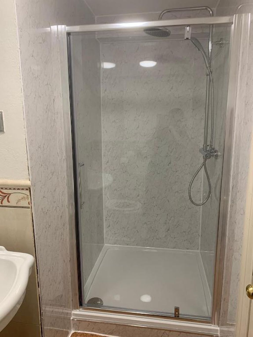 A glass-enclosed shower stall with a handheld showerhead and a wall-mounted faucet.