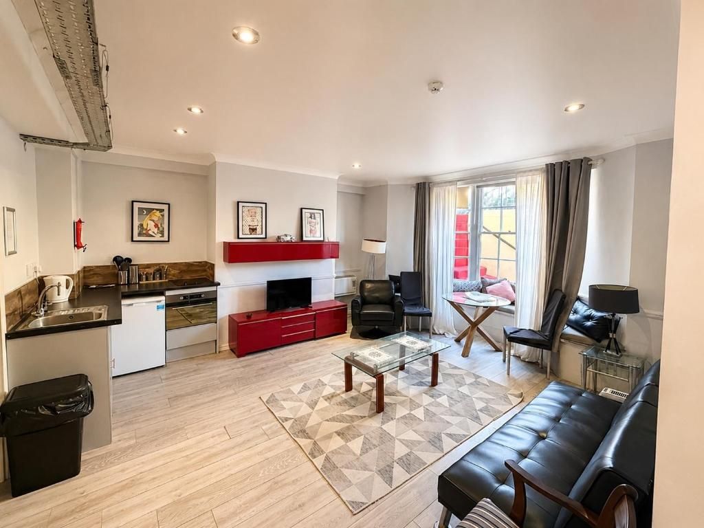 Un salon moderne avec un canapé, une table basse et un téléviseur. Il y a également un coin cuisine avec un meuble rouge et un petit réfrigérateur.