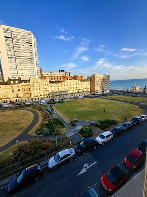 A coastal cityscape with a large building complex, a parking lot with cars, and a grassy area. - 12A Regency Square (Brighton)