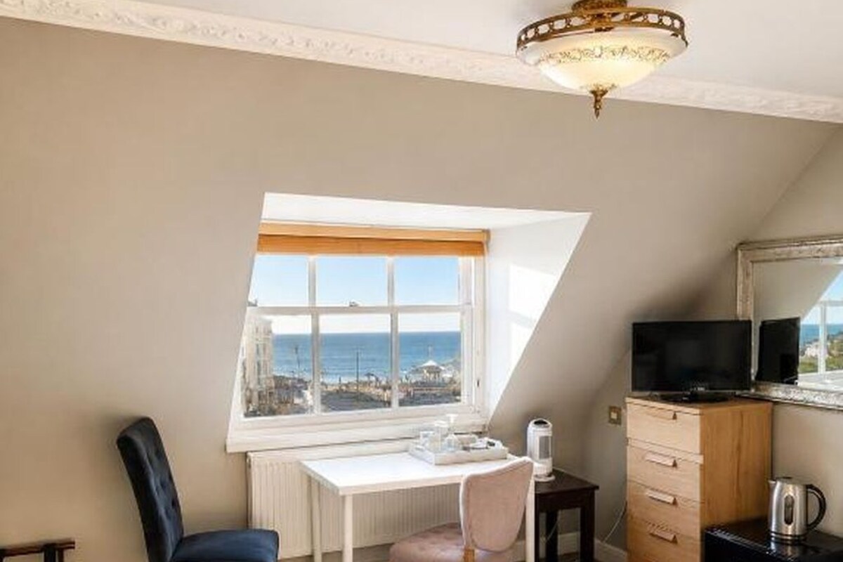 A bedroom with a bed, a desk, a chair, a television, and a view of the sea.