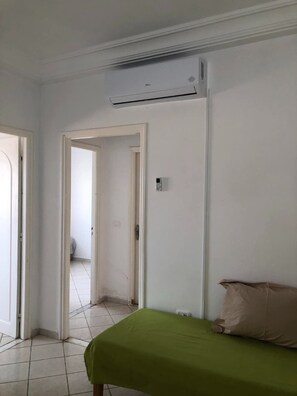 Ein Zimmer mit einem Bett, einer Klimaanlage, einer Tür und einem Fliesenboden.