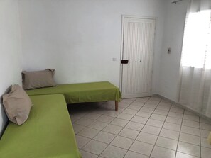 Ein kleines, sauberes Zimmer mit zwei Einzelbetten, einer weißen Tür und einem Fliesenboden.
