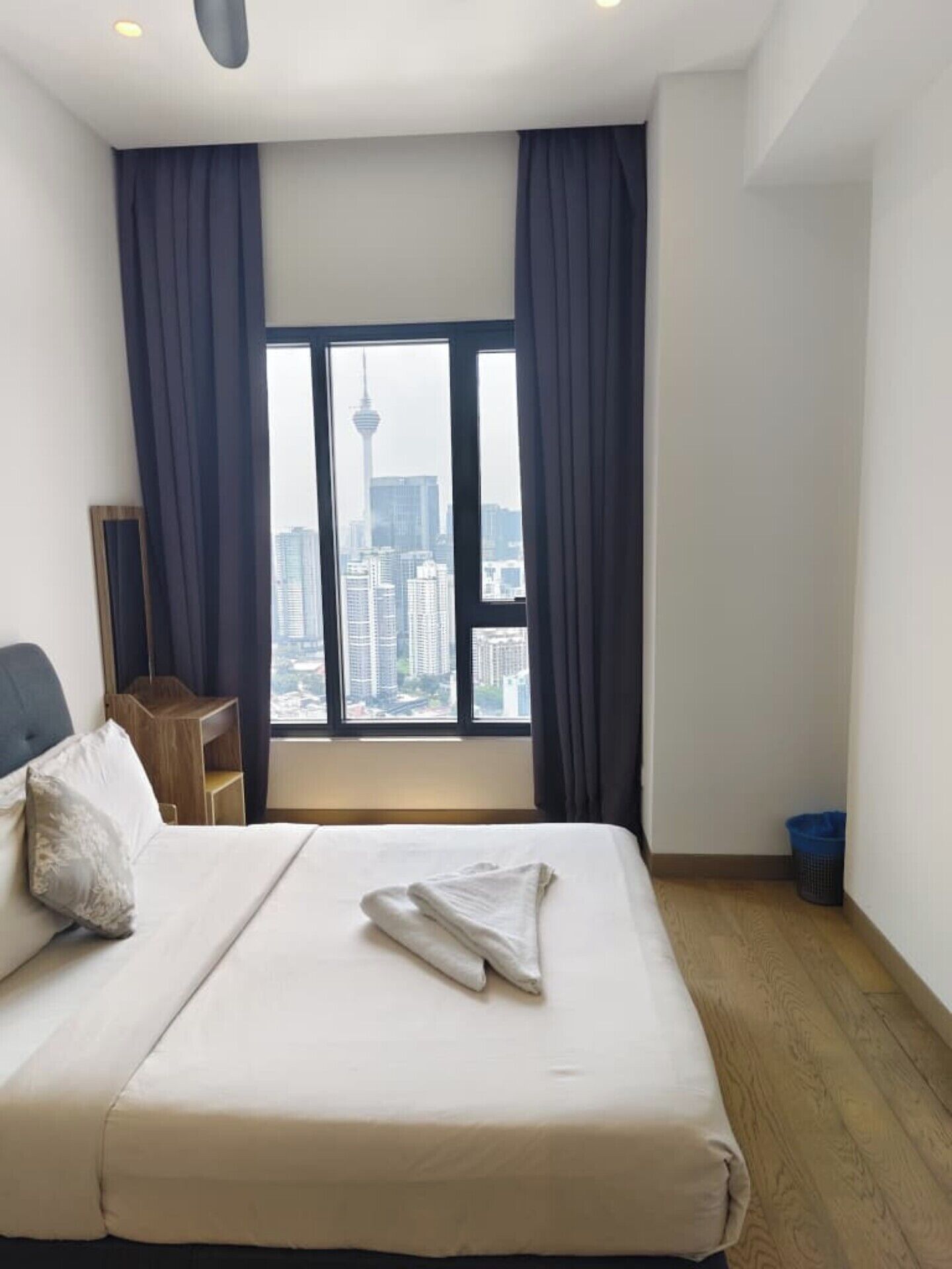 A hotel room with a bed, a small table, a chair, a window with curtains, and a view of a cityscape.