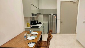 Une cuisine compacte comprenant un réfrigérateur, une table à manger avec des chaises et un petit plan de travail avec une bouilloire et d’autres ustensiles.