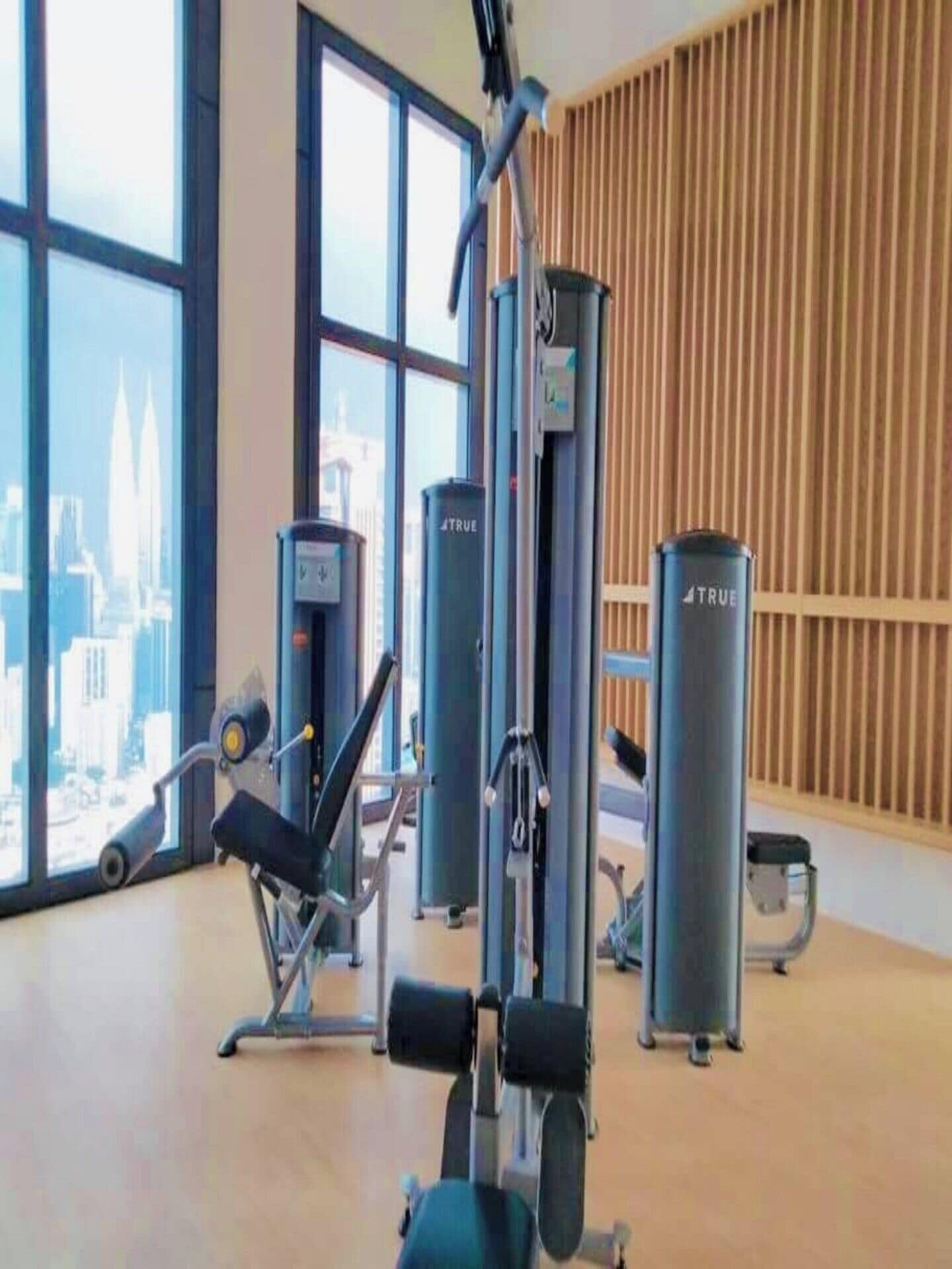 Ett gym med träningsutrustning, stora fönster och utsikt över en stad.