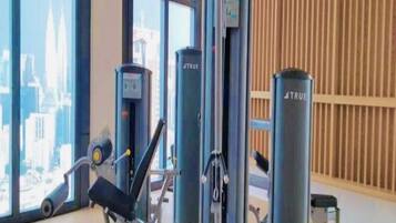 Ett gym med träningsutrustning, stora fönster och utsikt över en stad.