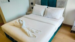 Un lit bien fait, avec du linge de lit blanc et une serviette, une tête de lit agrémentée d’une touche de couleur turquoise et un plancher en bois.