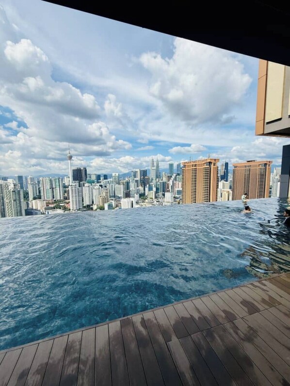 An infinity pool with a city skyline view, wooden deck, and modern buildings.