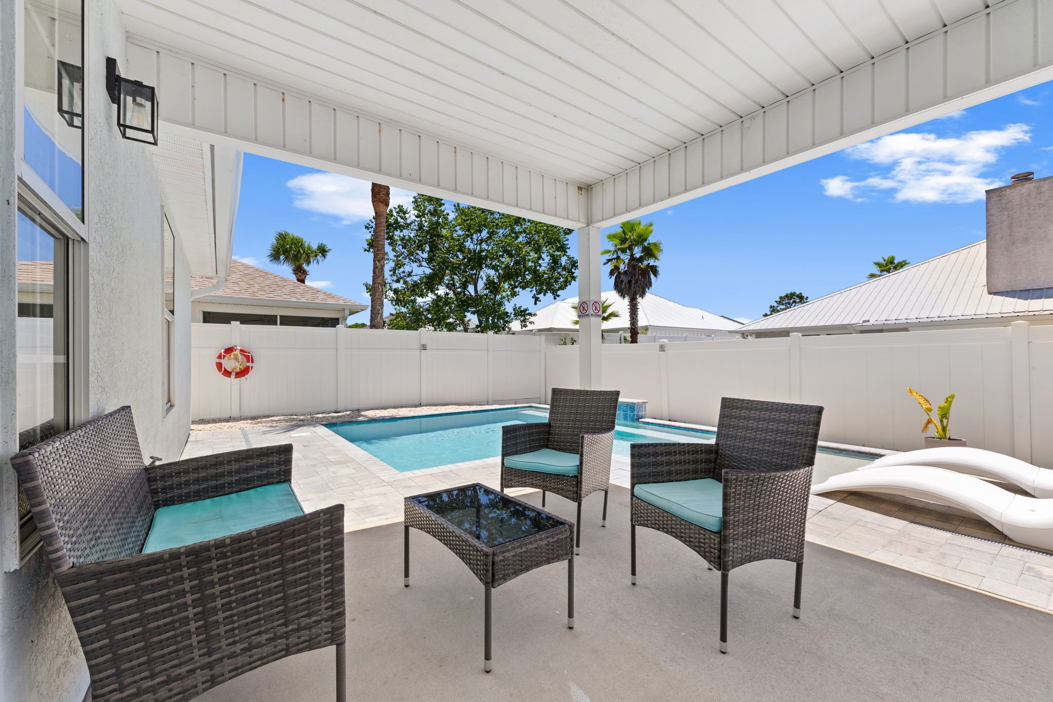 An outdoor patio with a pool, wicker furniture, and a covered area.
