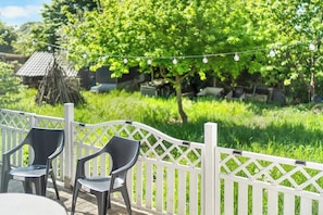 An outdoor seating area with chairs and a table, surrounded by a white fence and greenery.