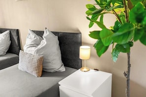 A bed with pillows, a bedside table with a lamp, and a plant.