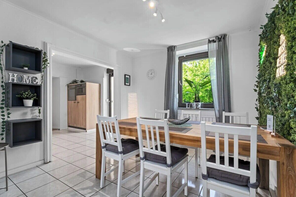 Een moderne keuken met een houten tafel, witte stoelen en uitzicht op groen.