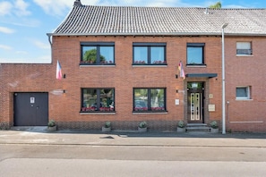 A two-story brick building with a tiled roof, a black door, and windows with flower boxes. - Brick-Lane by Loftigo - Patio & Sunroom (Selfkant)