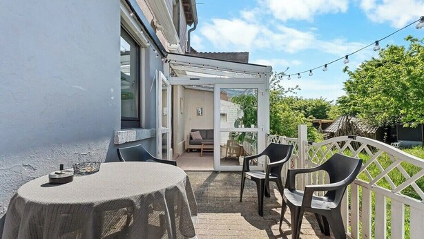 A patio with a table and chairs, a white fence, and a view into a house. - Brick-Lane by Loftigo - Patio & Sunroom (Selfkant)