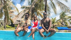 Three people sitting by a pool with palm trees in the background. - Relaxing 4-bedroom beach house at Malindi sand dunes perfect for family getaway (Mambrui)