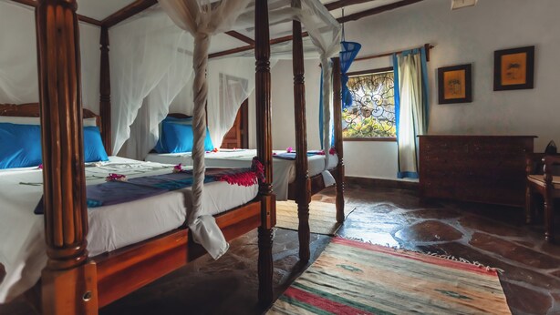 A four-poster bed with white linens, a wooden floor, and a view of greenery outside. - Relaxing 4-bedroom beach house at Malindi sand dunes perfect for family getaway (Mambrui)