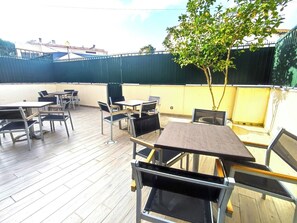 An outdoor patio with tables and chairs, a tree, and a view of buildings in the background. - Lisbon Airport GuestHouse Gal – Twin Bedroom (Lisbon)