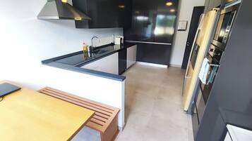 A modern kitchen with a black countertop, stainless steel appliances, and a wooden bench.