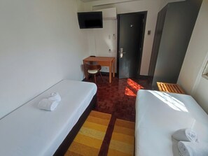A hotel room with two beds, a desk, a chair, a television, and a door. - Lisbon Airport GuestHouse Gal – Twin Bedroom (Lisbon)