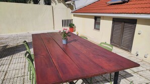 Ein Holztisch mit Stühlen, einer Topfpflanze und einem kleinen Fenster mit Fensterläden.