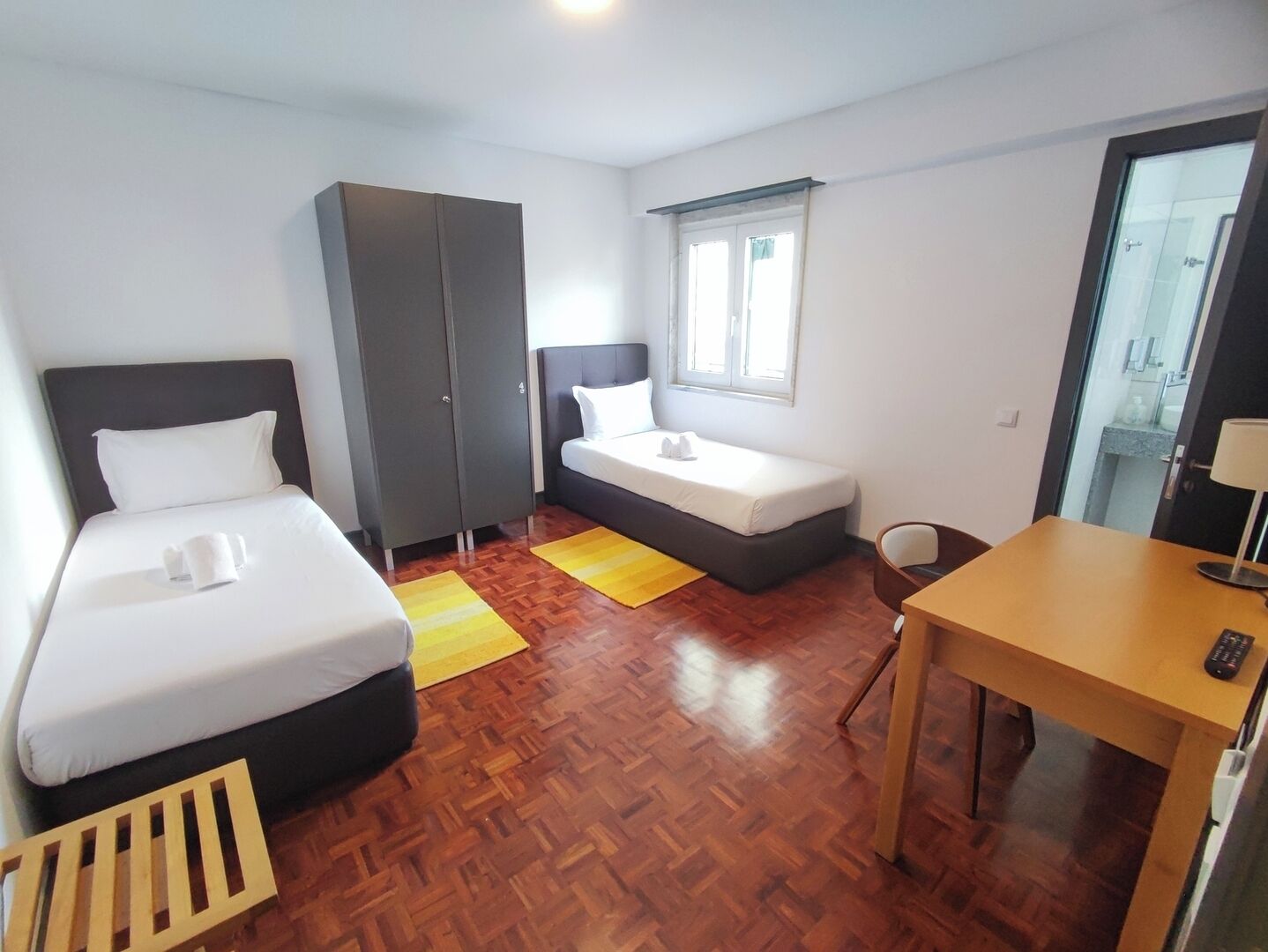 A hotel room with two beds, a desk, a wardrobe, and a window.