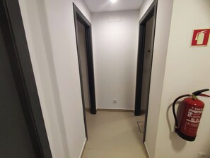 A narrow hallway with white walls and black doors, a fire extinguisher mounted on the right wall, and a ceiling light. - Lisbon Airport GuestHouse Gal – Twin Bedroom (Lisbon)