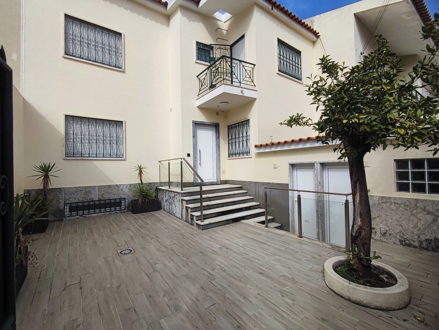 A multi-story building with a staircase leading to a balcony, potted plants, and a tree in the courtyard.