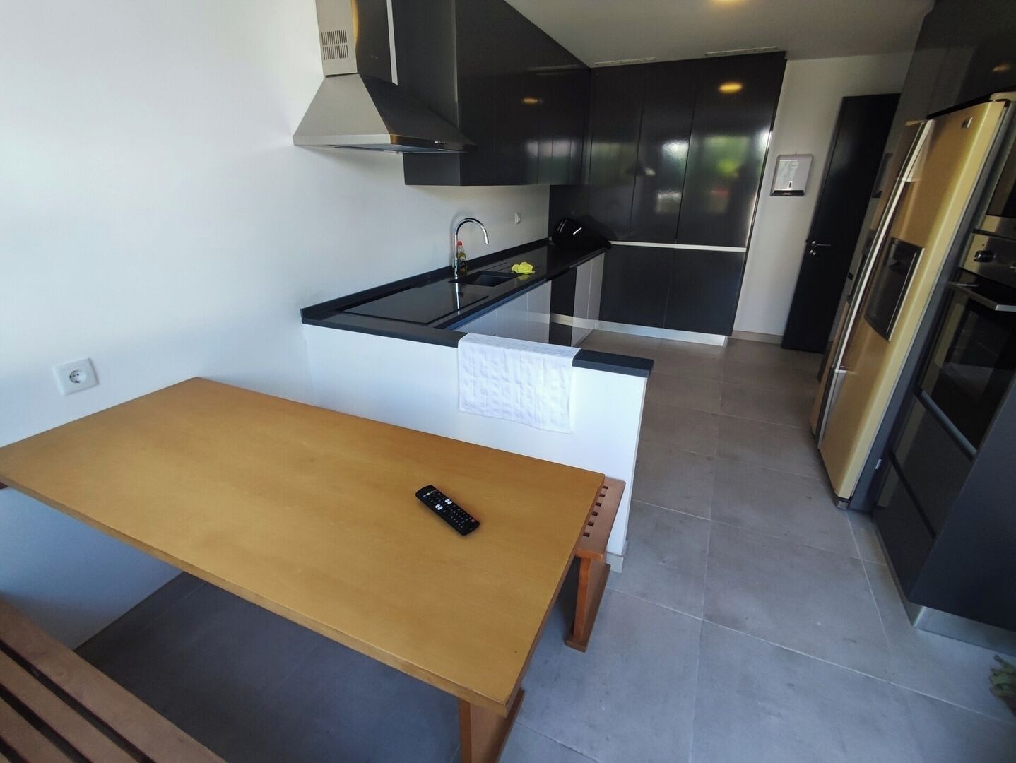 A modern kitchen with a wooden table, a black countertop, and stainless steel appliances.
