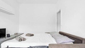 Habitación de hotel minimalista con cama, televisor, mesita de noche y un cartel que dice 'HOME'.
