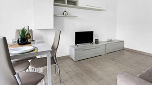 Una sala de estar moderna con comedor, un televisor de pantalla plana y estanterías empotradas.