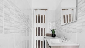 Un baño moderno con lavamanos blanco, espejo y planta en maceta.