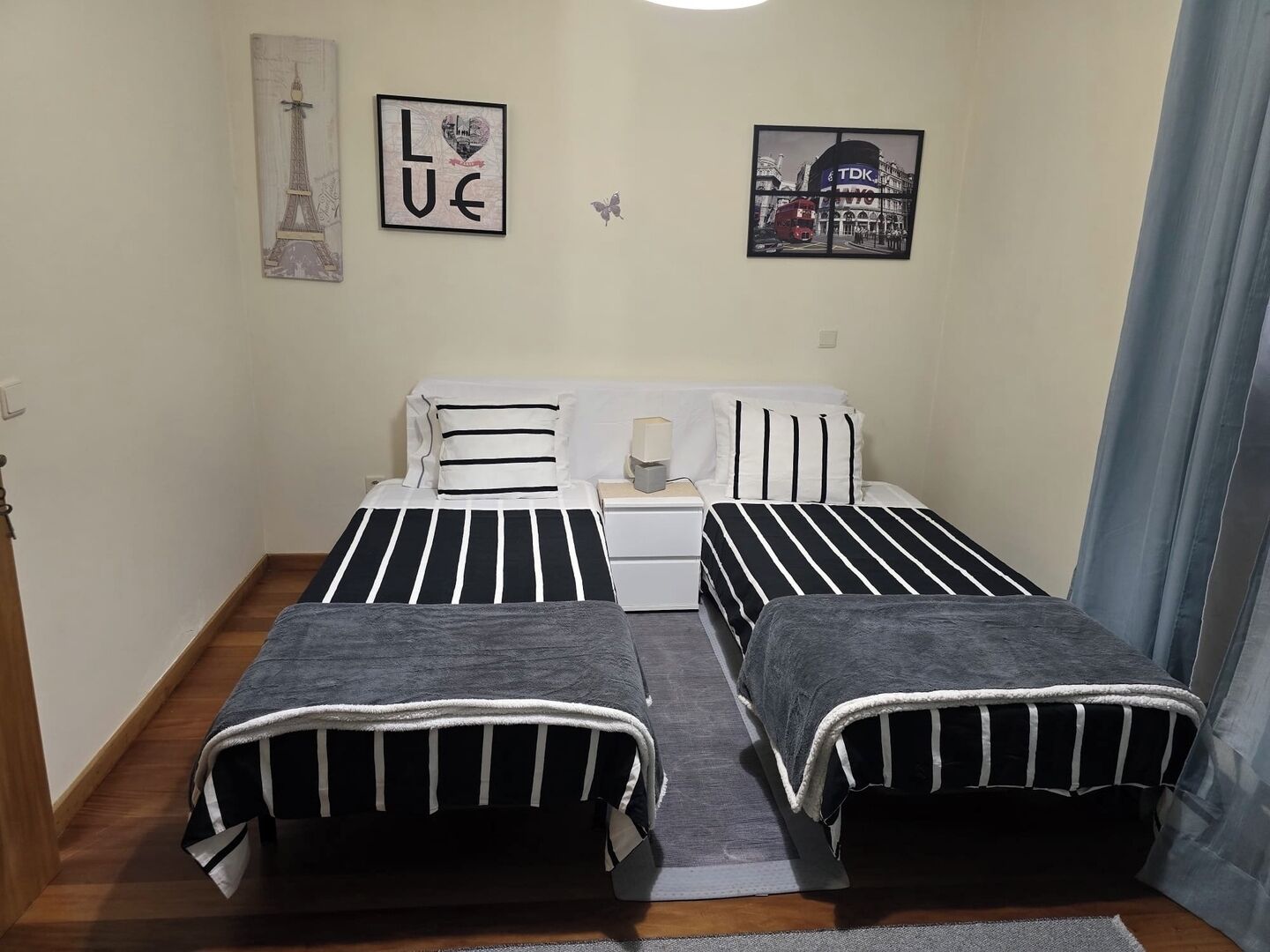 A bedroom with two beds, a nightstand, a lamp, and two wall-mounted pictures.