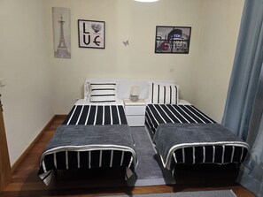 Quarto com duas camas, uma mesinha de cabeceira, um abajur e duas imagens penduradas na parede.