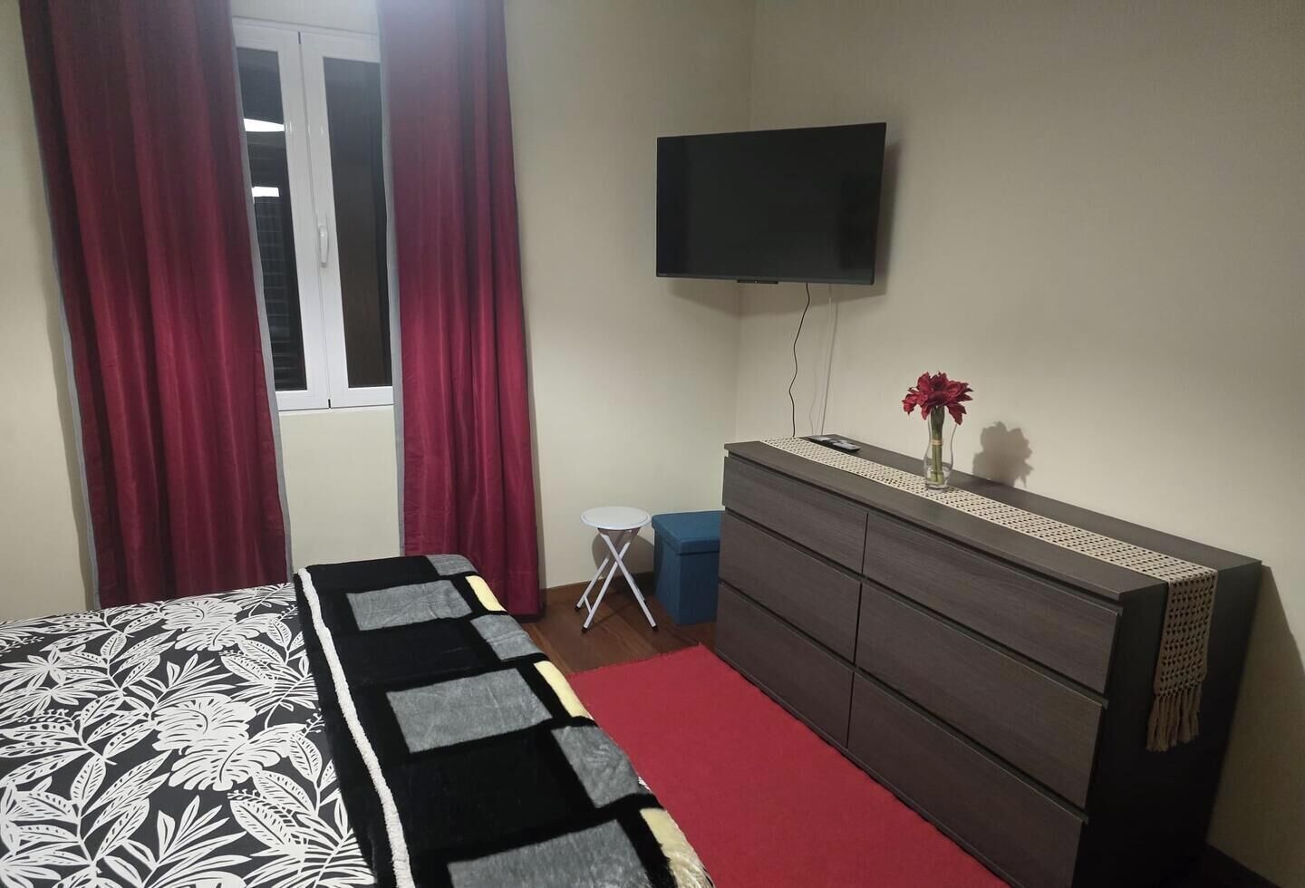 Ein Schlafzimmer mit einem Bett, einem Schminktisch, einem Fernseher und einem Fenster mit Vorhängen.