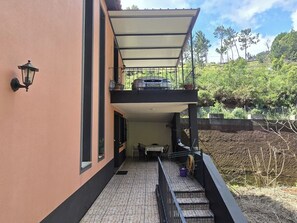 Un bâtiment à deux étages doté d’un balcon couvert, une voiture garée au niveau supérieur et une vue sur un paysage verdoyant.