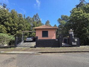 A small building with a tiled roof, a gated entrance, and a car parked in front. - Madeira, 2 Bedroom Nature Retreat near Santa Cruz (Gaula)